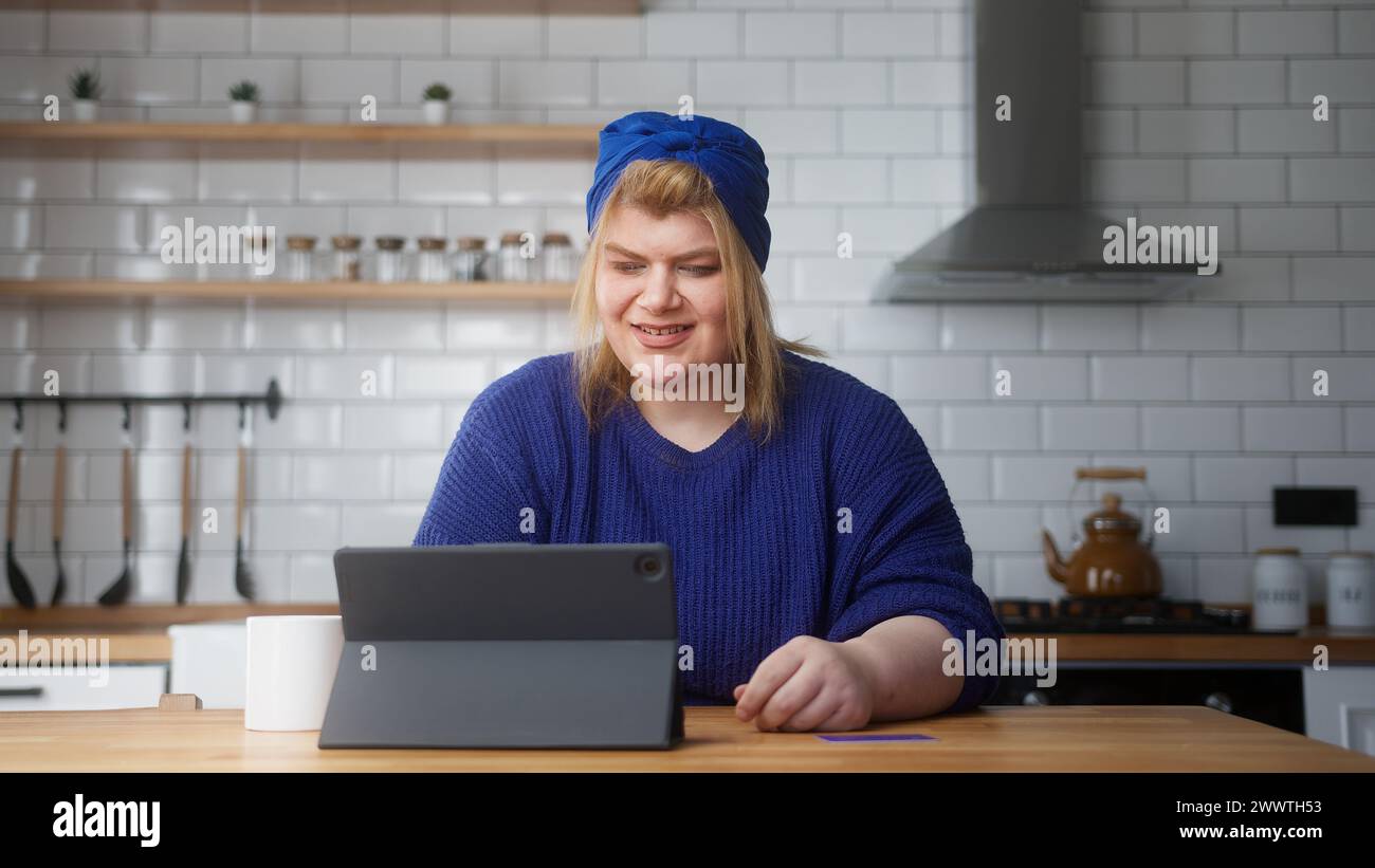 Donna sorridente in sovrappeso inserire il numero di carta di credito sul tablet per fare acquisti online, rende sicuro e facile il pagamento elettronico a distanza mentre sono seduto Foto Stock