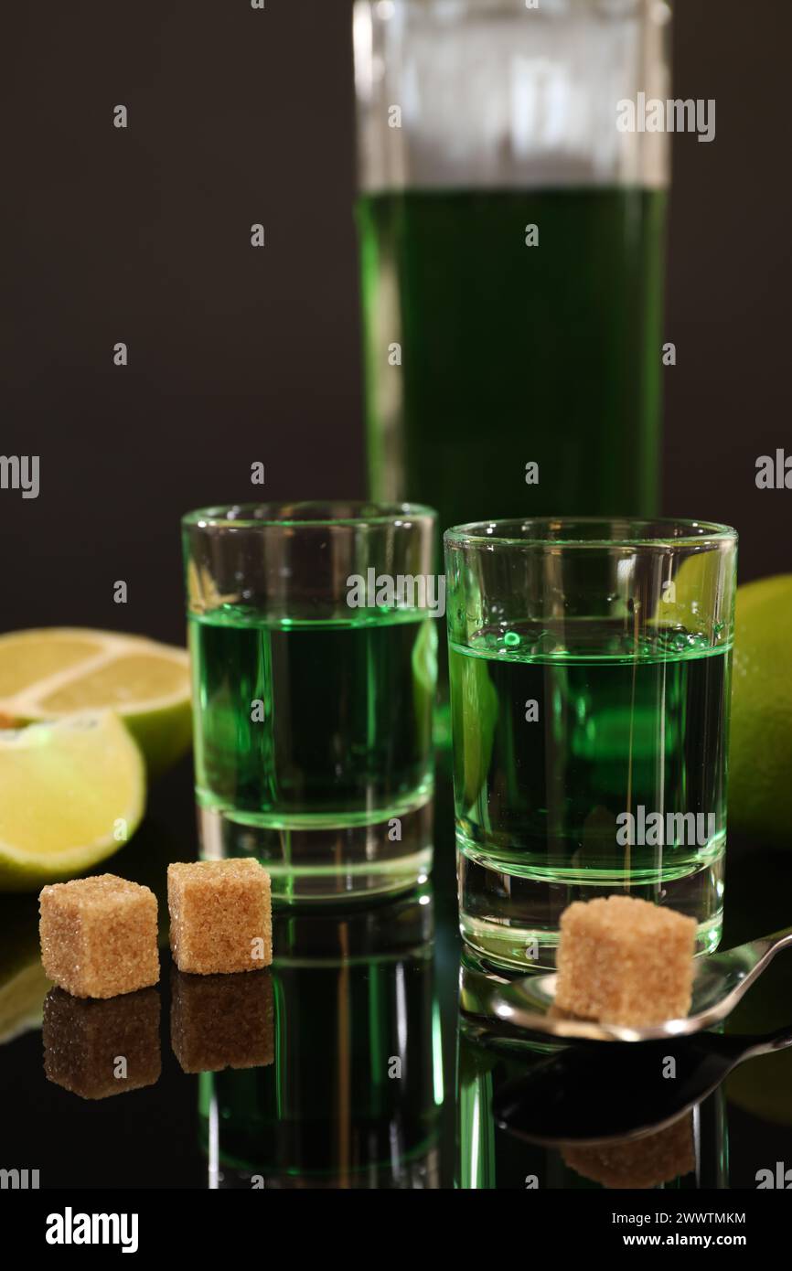 Absinthe in bicchieri da shot, zucchero di canna, lime e cucchiaio sul tavolo a specchio. Bevanda alcolica Foto Stock