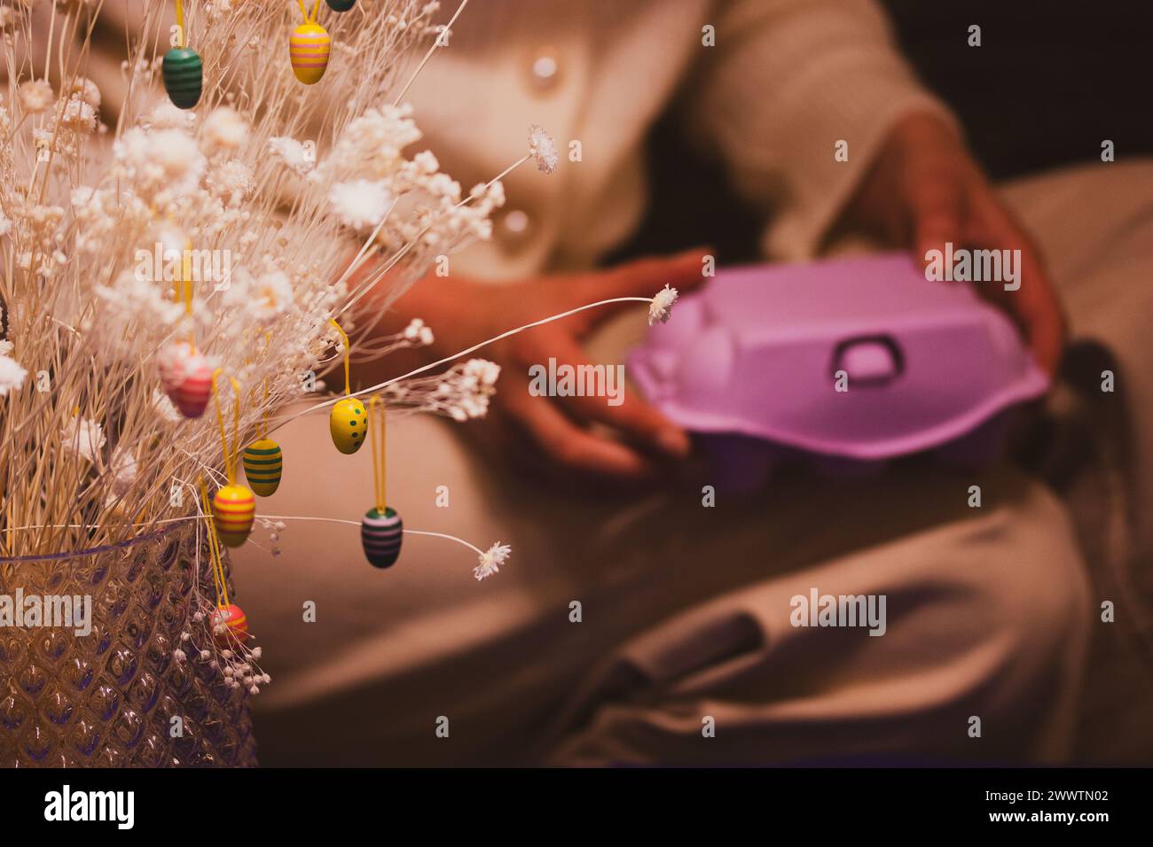 Collezione di uova di Pasqua splendidamente dipinte e una scatola di cartoni animati viola con uova in mano alla donna. Scatola di uova chiusa con biglietti d'auguri natalizi dai colori vivaci Foto Stock