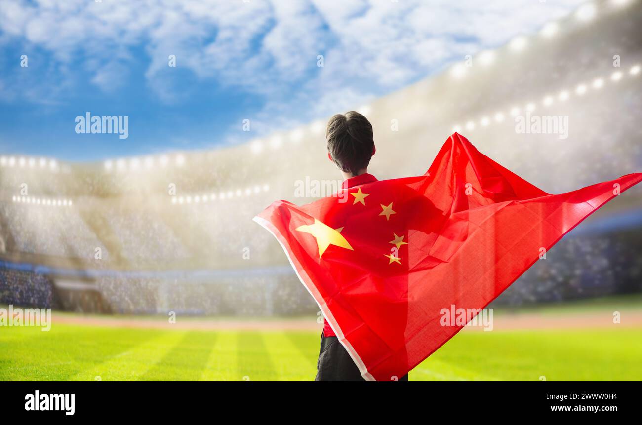 Tifoso di calcio cinese allo stadio. Tifosi cinesi sul campo da calcio che guardano le partite di squadra. Gruppo di tifosi con bandiera e maglia nazionale che tira Foto Stock
