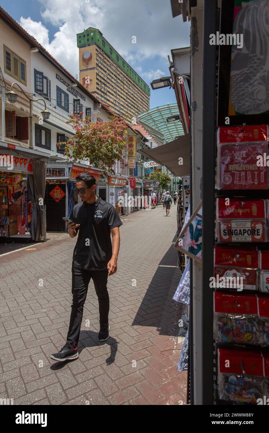 La vista verticale di un uomo in camicia nera cammina lungo Chinatown Street sotto il sole caldo a metà pomeriggio. Singapore. Foto Stock