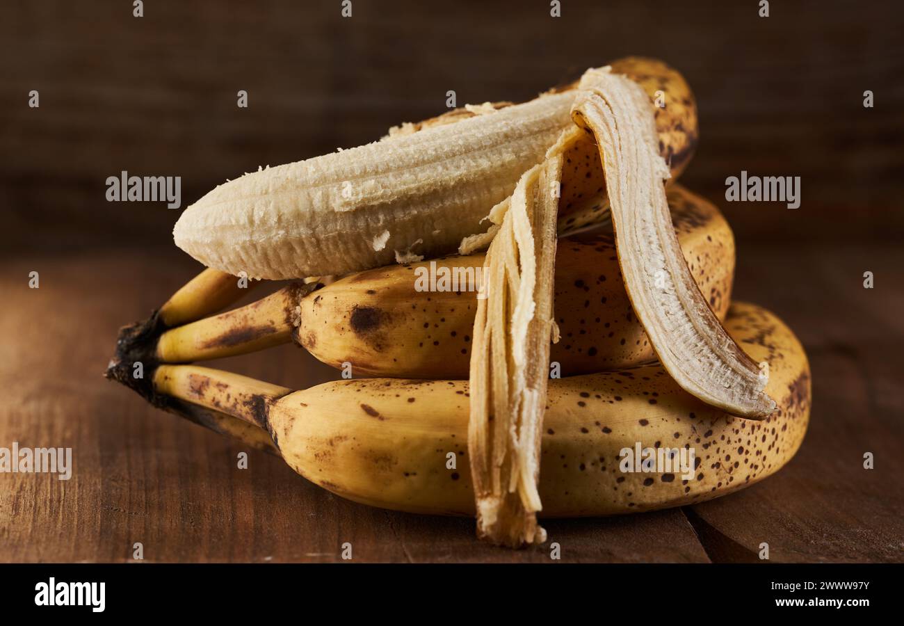Mazzo di banane dolci troppo maturi su un rustico asse di legno Foto Stock