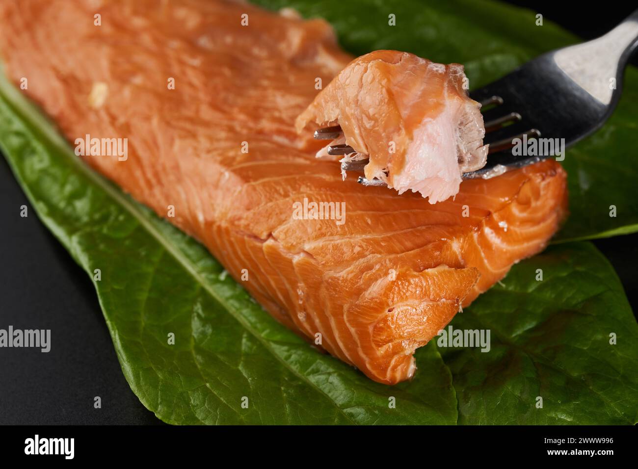 Salmone affumicato su foglie di lattuga in primo piano su sfondo nero Foto Stock