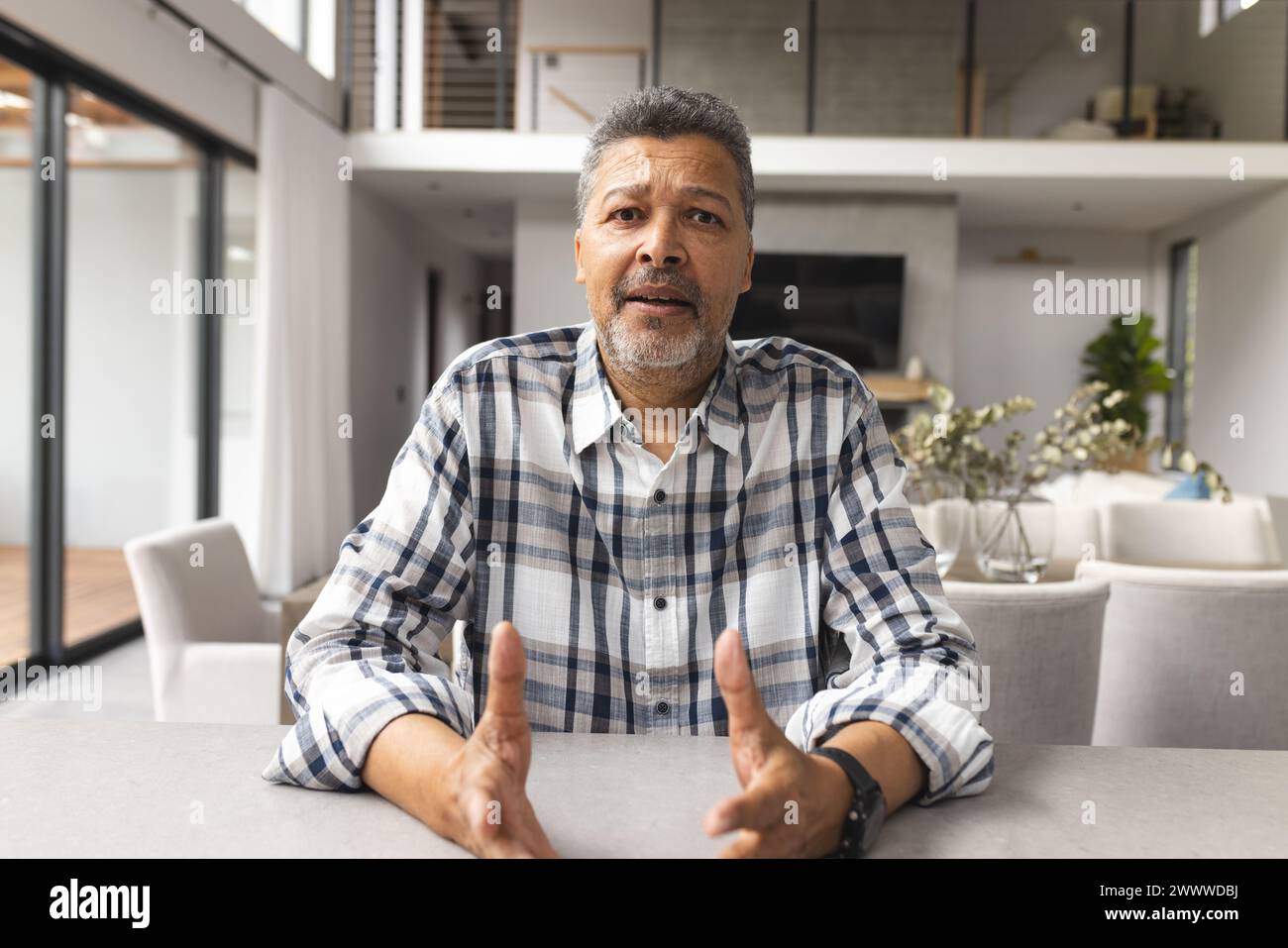 Un uomo birazziale di mezza età è seduto a un tavolo in un video a casa Foto Stock