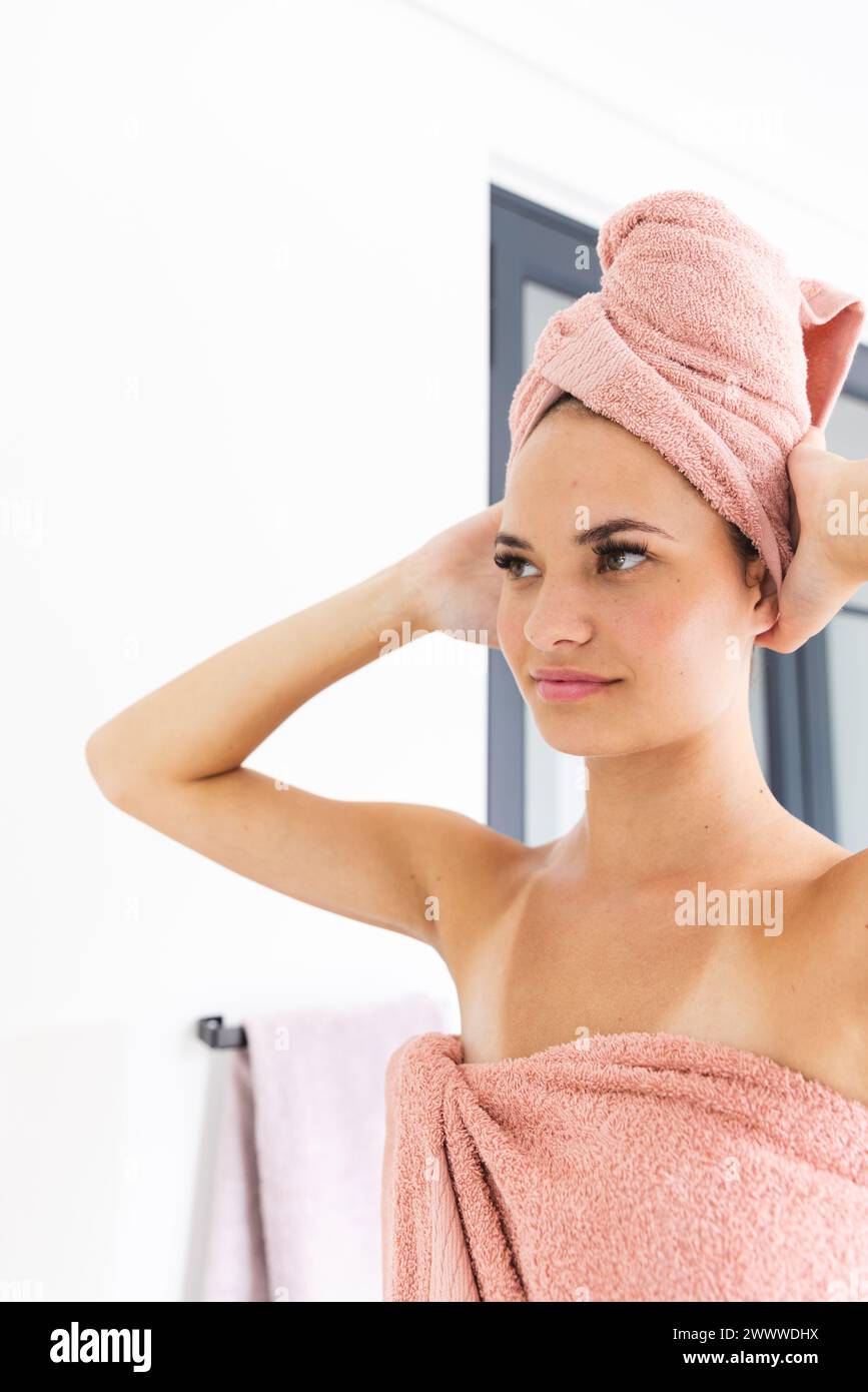 Una giovane donna caucasica avvolta in un asciugamano sembra penosa in un bagno di casa Foto Stock
