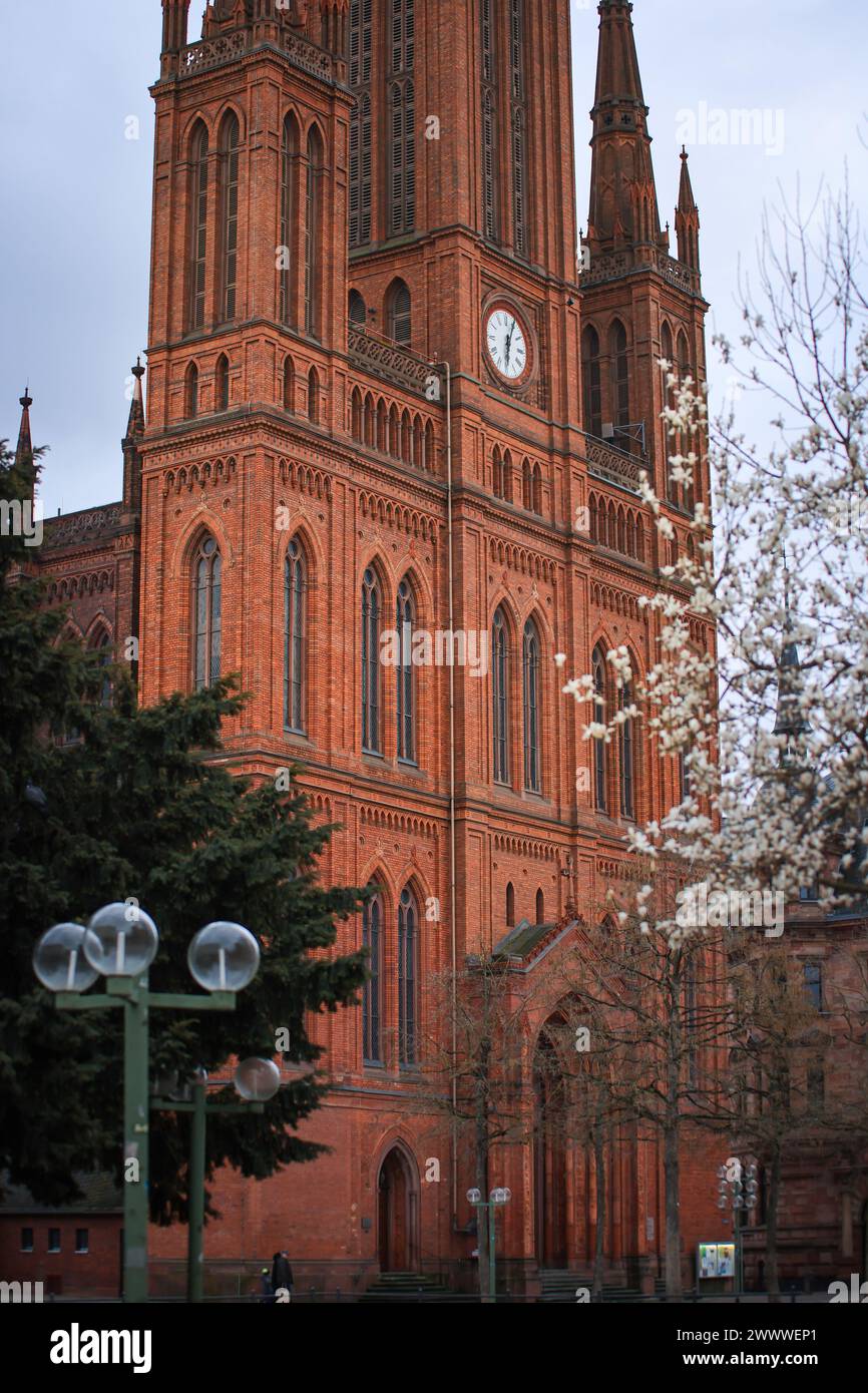 Torre dell'orologio della chiesa in primavera con alberi in fiore e cielo nuvoloso a Wiesbaden Germania Foto Stock