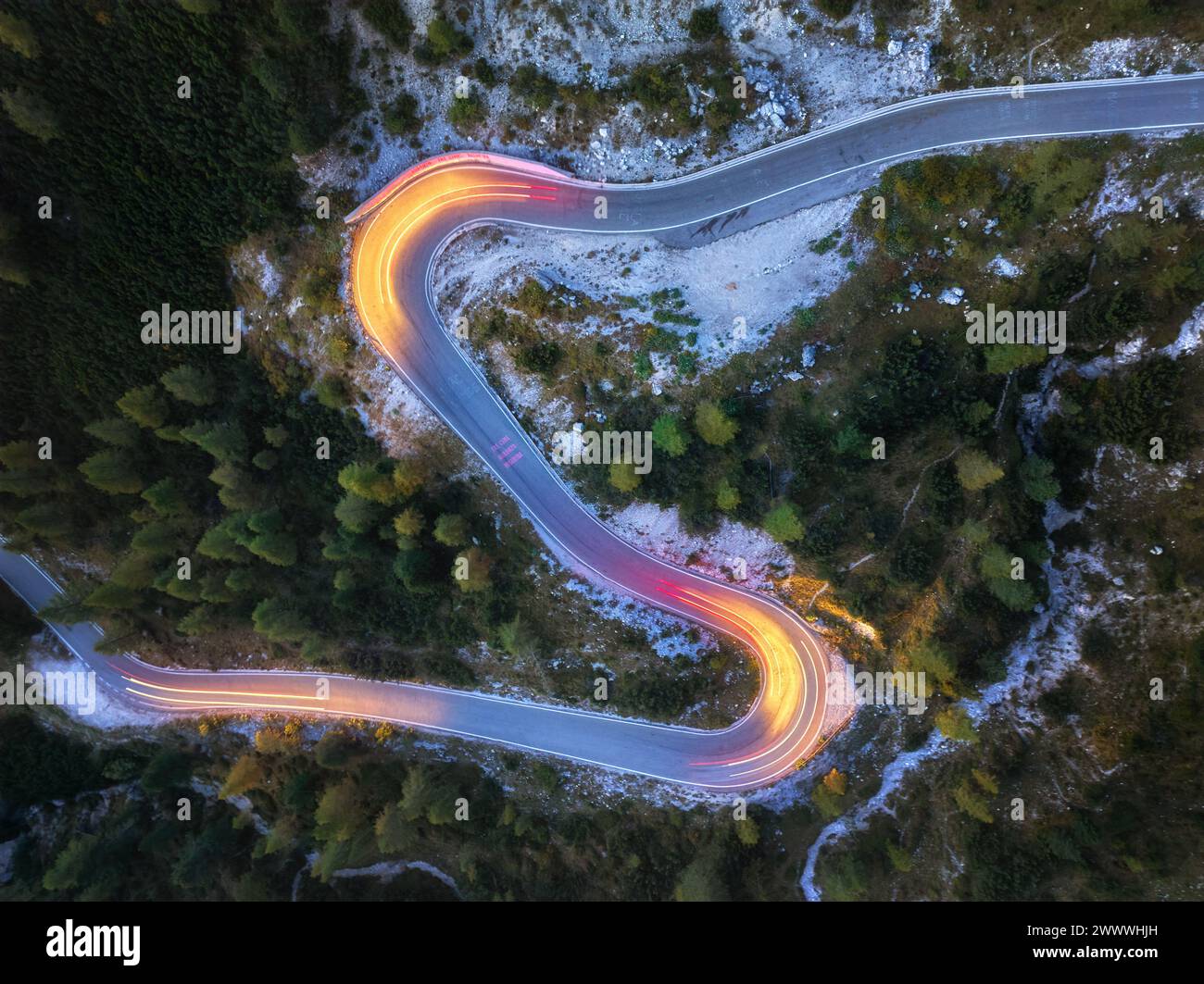 Una vista perpendicolare di una strada tortuosa con tracce di luci di passaggio per auto. Fotografia a lunga esposizione. Linee gialle e rosse, vista serale, strada di montagna. Foto Stock