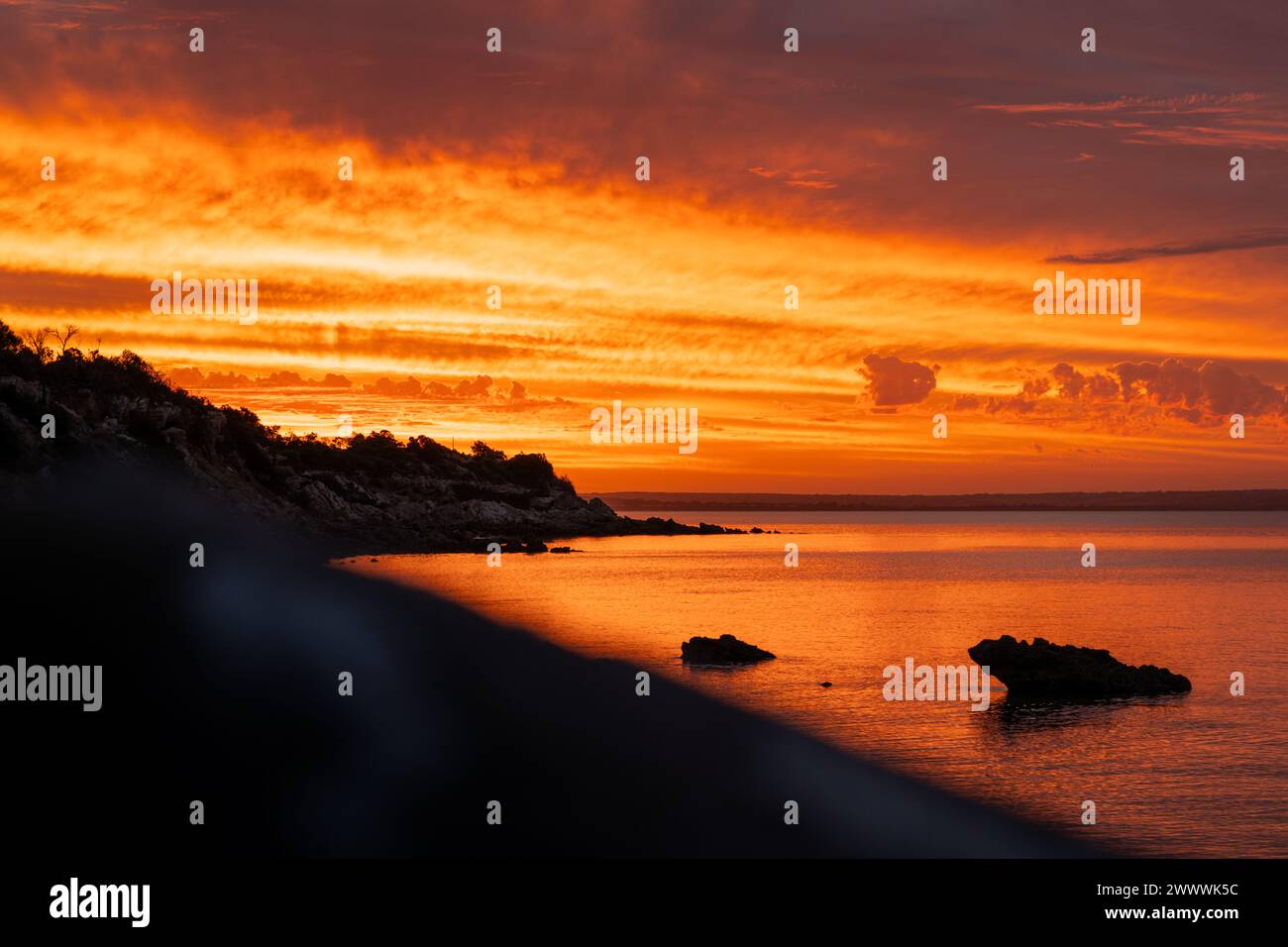 Il sole sorge sulla spiaggia oceanica con rocce in acqua Foto Stock