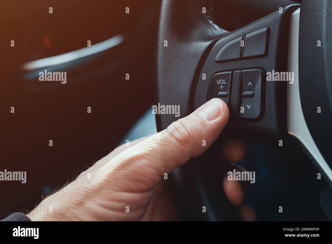 Il conducente preme il pulsante di riduzione del volume sul volante dell'auto, messa a fuoco selettiva Foto Stock