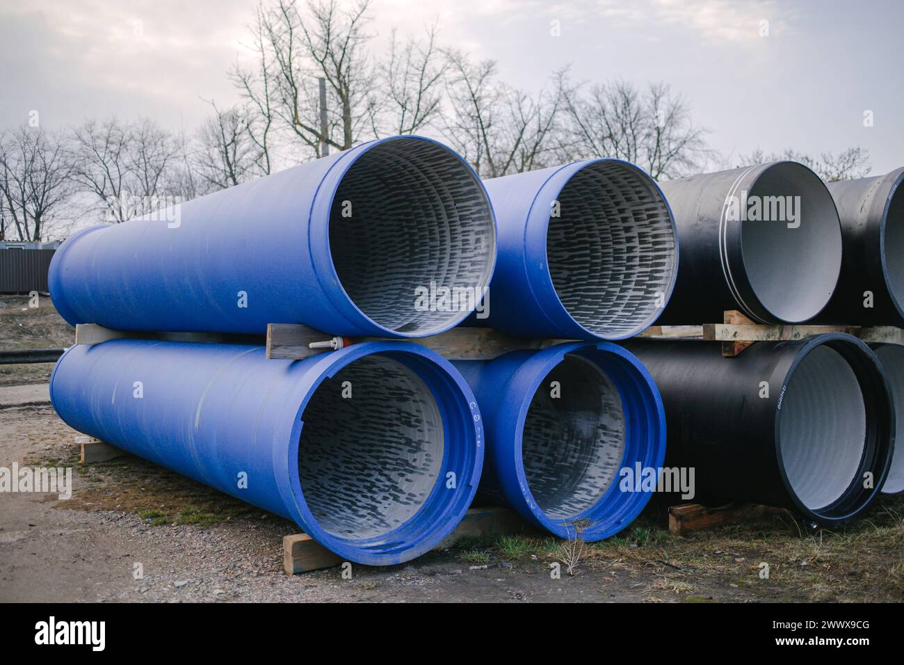 Grandi tubi industriali blu e neri impilati in un cantiere con alberi sullo sfondo Foto Stock