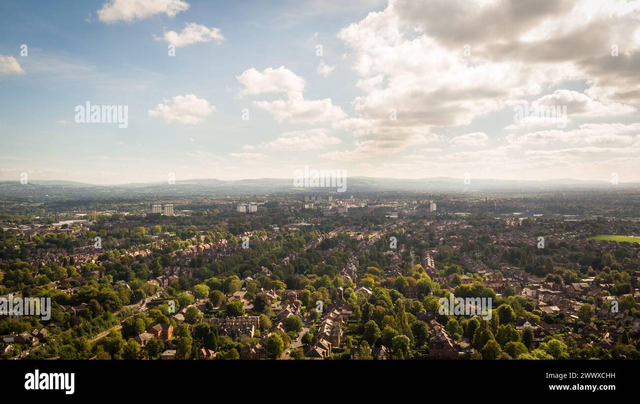 Immagine di un drone aereo scattata in una giornata di sole sopra Stockport guardando verso i sobborghi verdi con il Peak District in lontananza Foto Stock