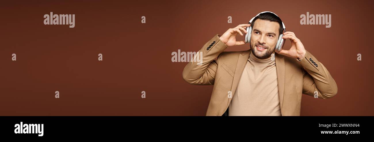 Uomo carismatico in un abbigliamento elegante che ascolta la musica con le sue cuffie wireless sul beige, banner Foto Stock