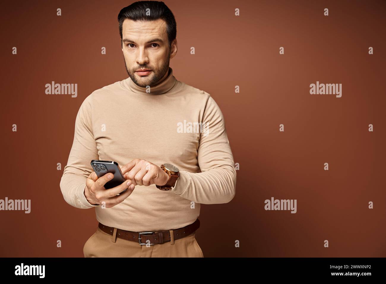 bell'uomo con setole dolcevita che usa il suo smartphone su sfondo beige, social media Foto Stock