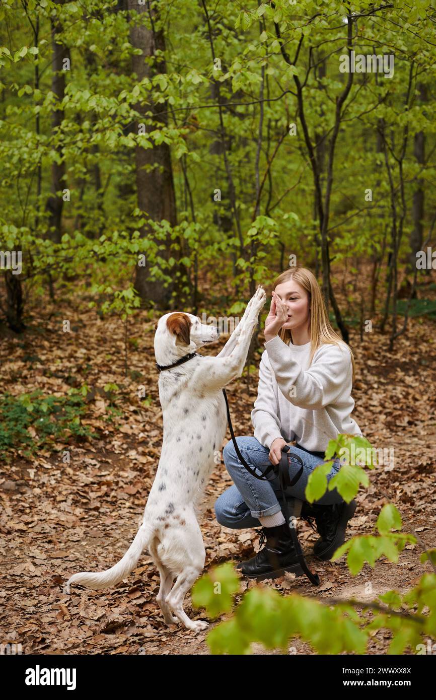 Un'escursionista sorridente con il suo cane da addestramento mentre fa trekking riposa con vista sulla foresta Foto Stock