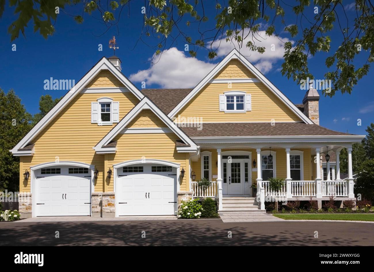 Casa di campagna contemporanea con finiture gialle e bianche con due garage, giardino panoramico e vialetto in asfalto nero in estate, Quebec, Canada Foto Stock