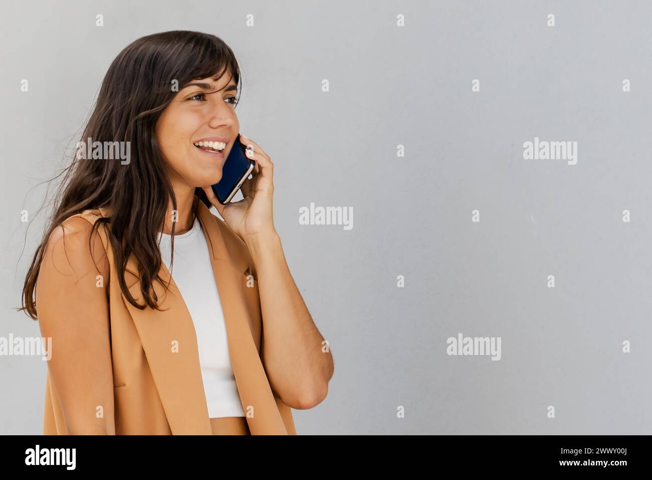 Una donna sta parlando al cellulare mentre indossa una giacca abbronzante. Lei sorride ed è di buon umore Foto Stock