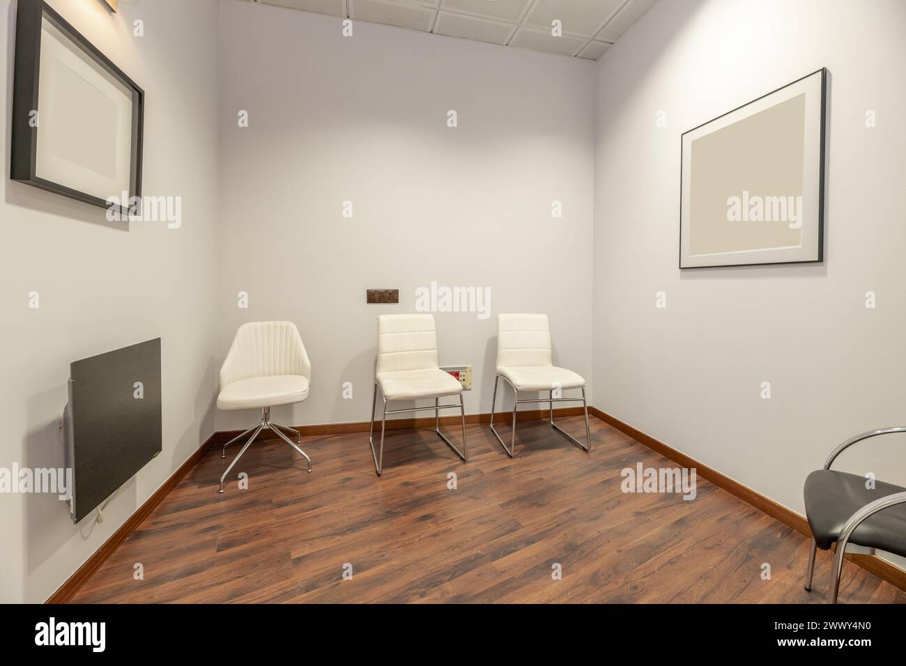 Un ufficio vuoto con semplici pareti dipinte di bianco, sedili imbottiti in skay bianco, pavimenti in parquet rossastro e soffitti tecnici Foto Stock