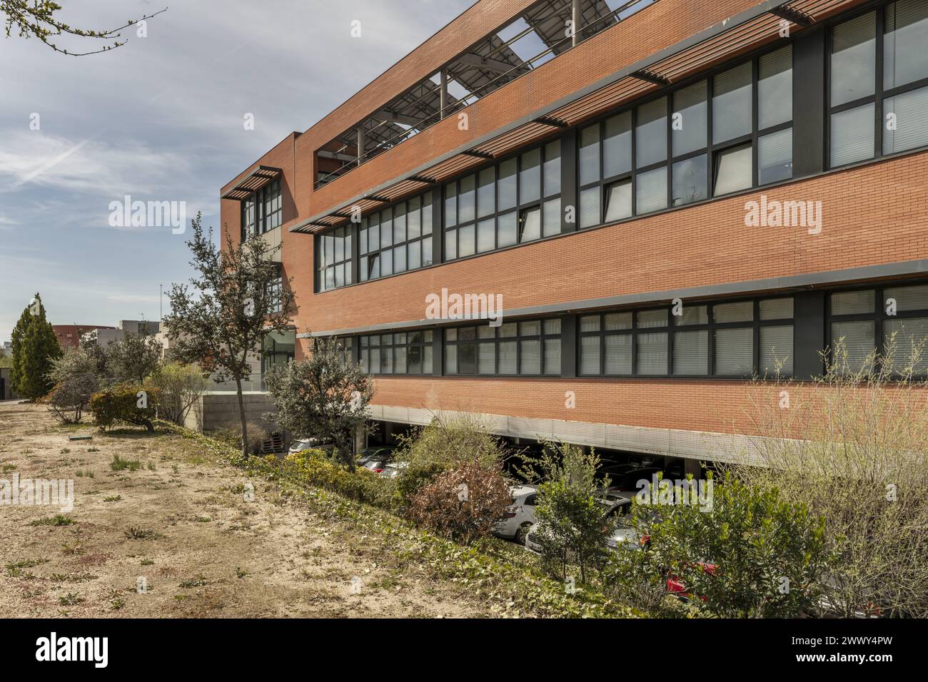 edificio per uffici con pareti in mattoni marrone chiaro combinato con finestre in metallo nero con parcheggio al piano terra Foto Stock