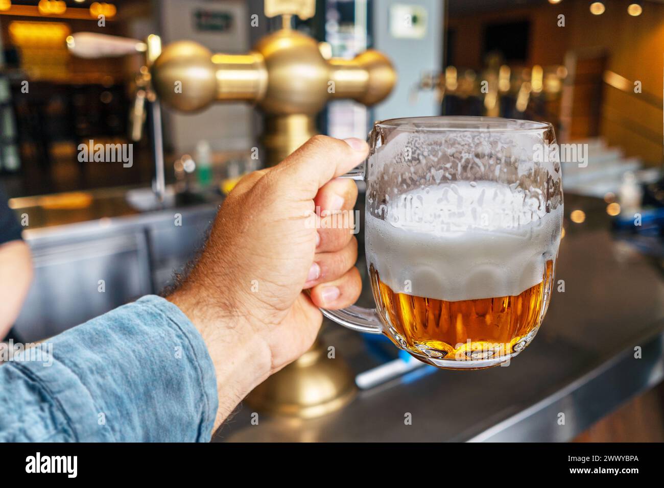 L'uomo tiene in mano la tazza di birra e spilli di birra di rame sullo sfondo. Foto Stock