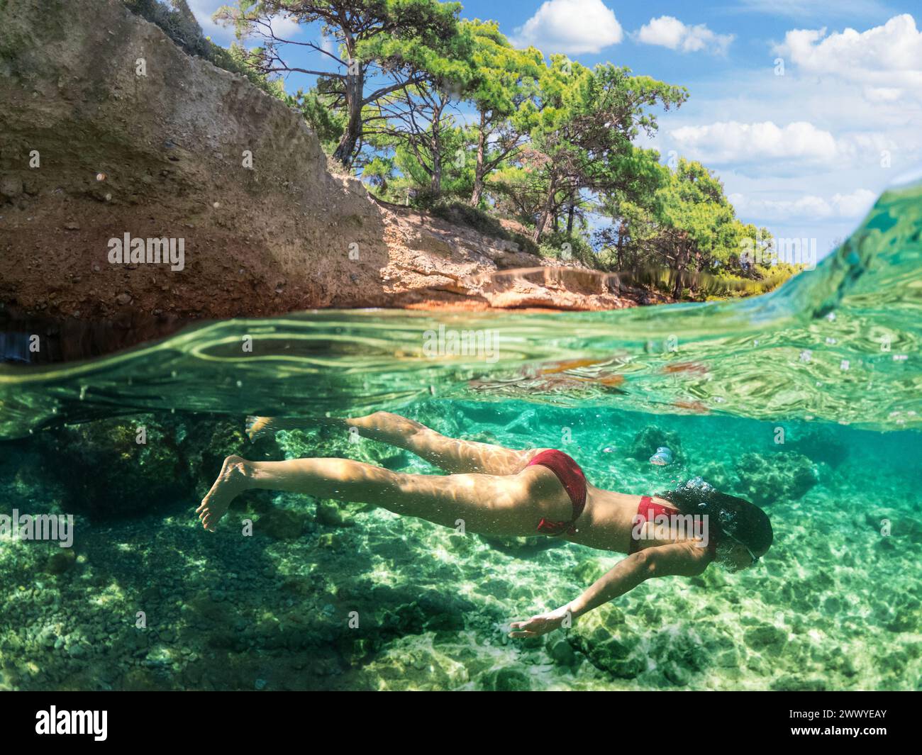 Donna subacquea sta facendo snorkeling su una bellissima spiaggia di mare. La metà inferiore dell'immagine è occupata dal fondale marino, la metà superiore dalla costa e dal cielo. Foto Stock