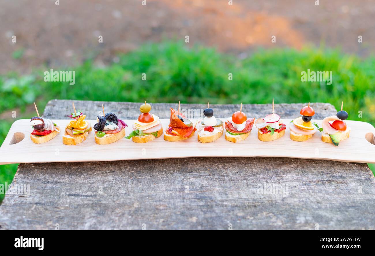 Finger food, vari canapè con verdure, prosciutto, pancetta, formaggio e olive su tavola di legno. Foto Stock