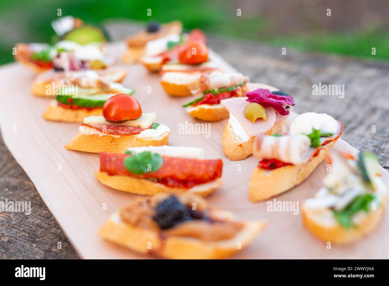 Finger food, vari canapè con verdure, prosciutto, pancetta, formaggio e olive su tavola di legno. Foto Stock