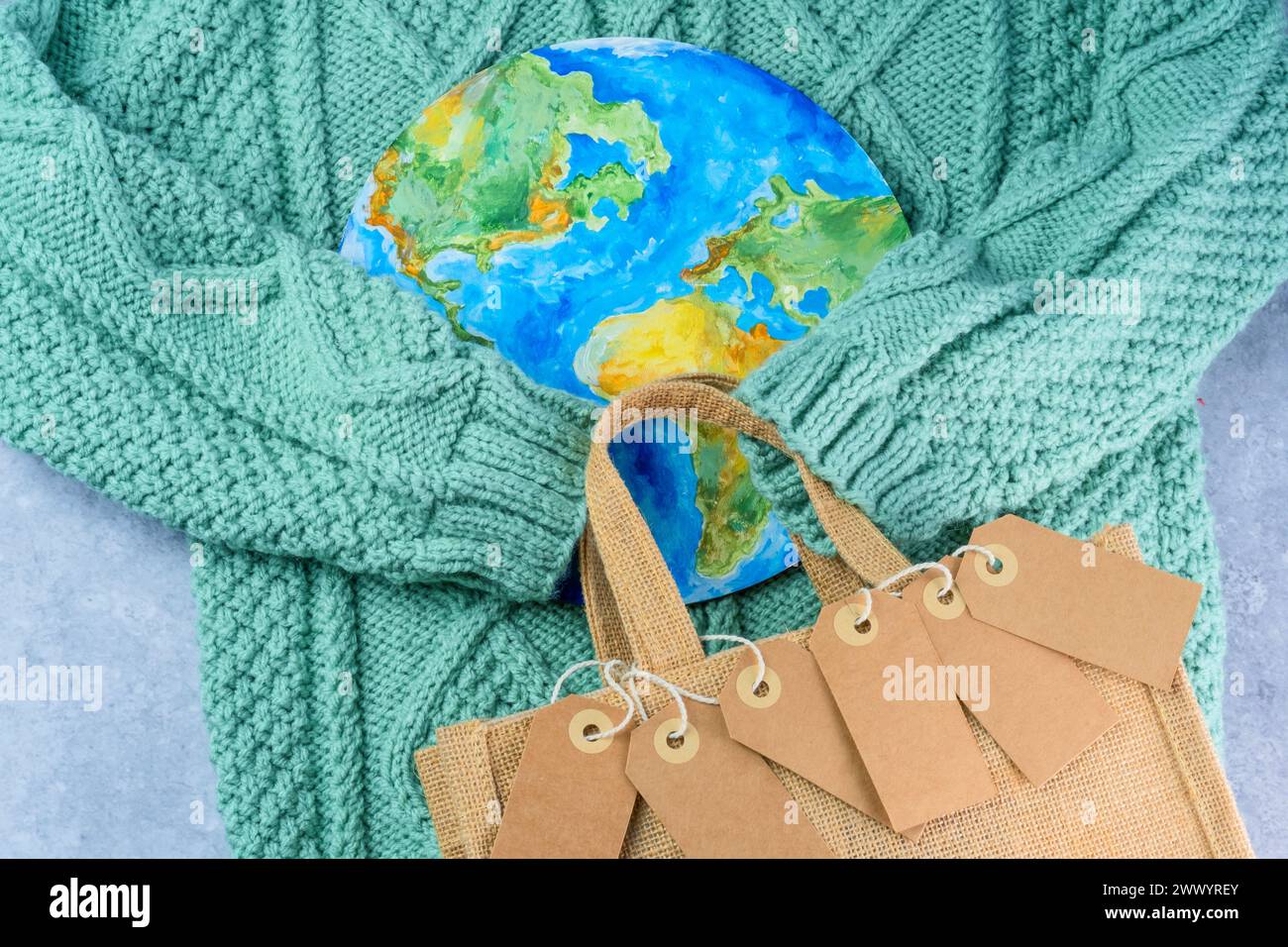 Le maniche del maglione che tengono le etichette nell'abbraccio del pianeta con una borsa ecologica. Consumo responsabile. Il concetto creativo acquista di meno Foto Stock