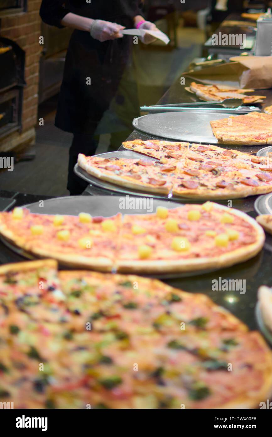 Questa immagine mostra una varietà di pizze fresche con diversi condimenti, pronte per essere servite. Le pizze sono disposte sul bancone di una pizzeria illuminata, Foto Stock