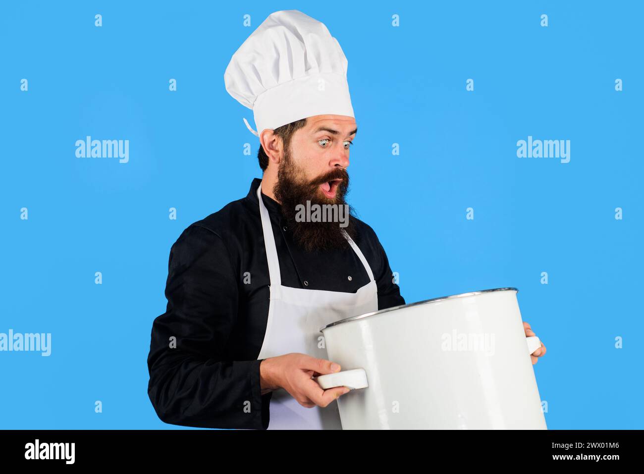 Cucinare il cibo. Uomo barbuto sorpreso con cappello da chef e uniforme con casseruola o casseruola. Cuoco maschile in grembiule con pentola grande o padella. Pentole Foto Stock
