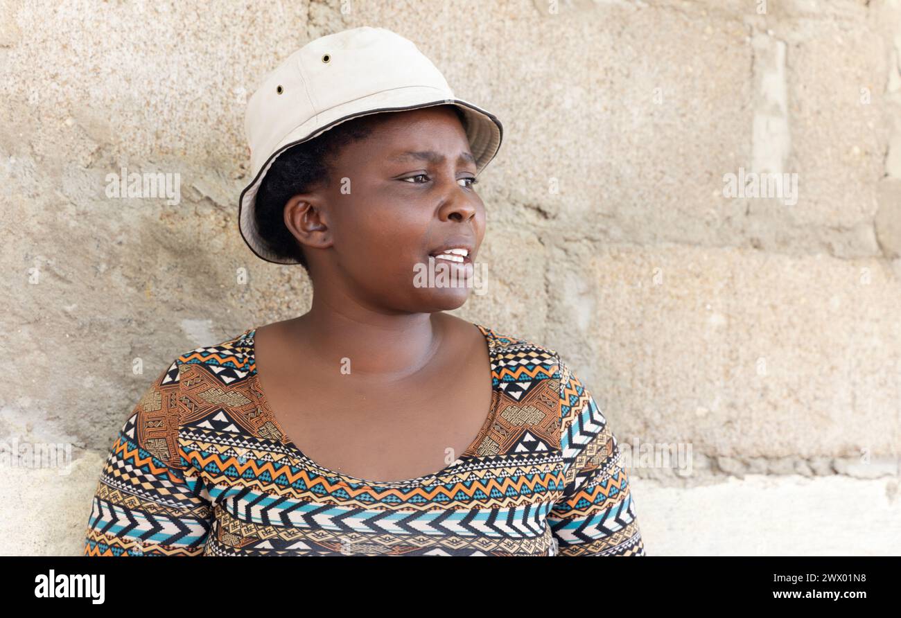 la giovane donna africana in piedi accanto a un muro indossa un cappello, la vita di villaggio Foto Stock