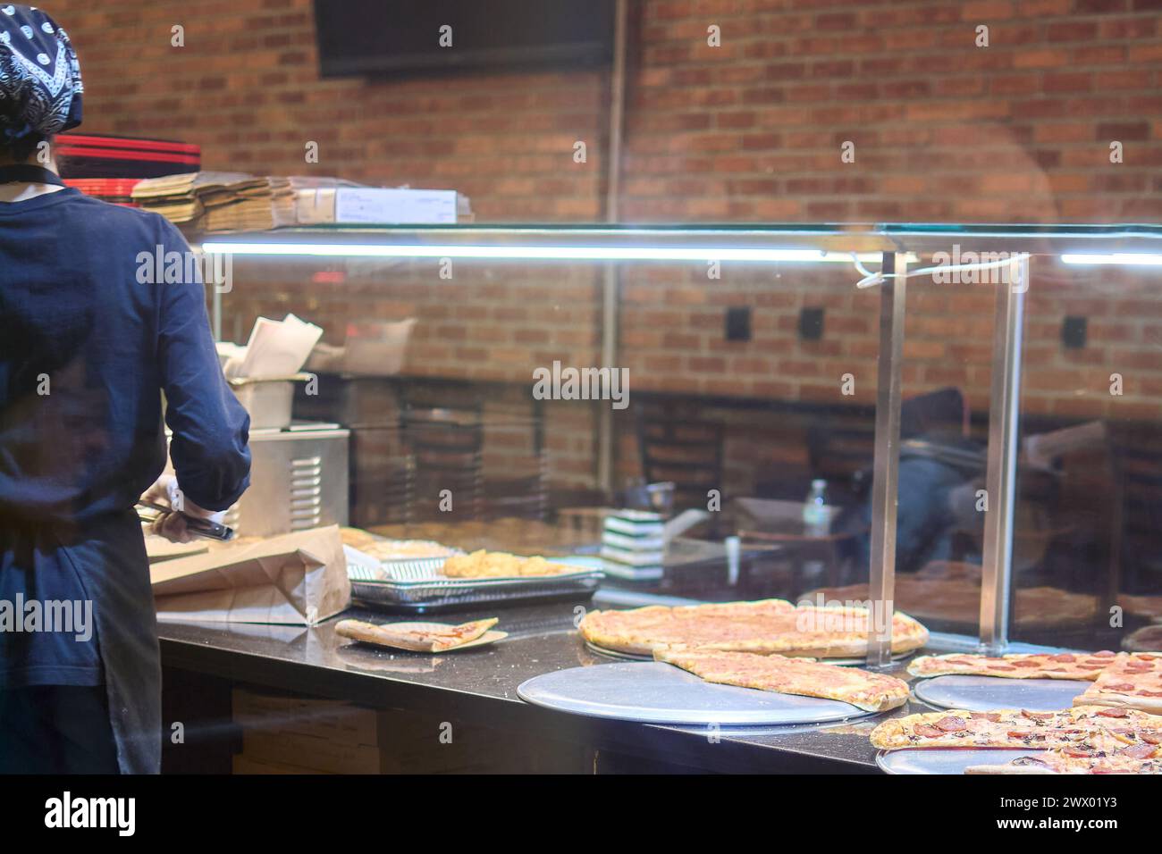 Lavoratrice in una pizzeria che prepara una varietà di pizze fresche da servire in un'atmosfera rustica e calda Foto Stock