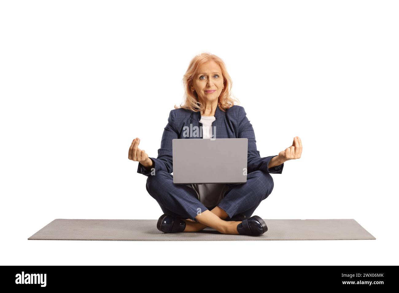 Donna d'affari matura con un computer portatile seduto su un tappetino per esercizi e meditando isolata su sfondo bianco Foto Stock