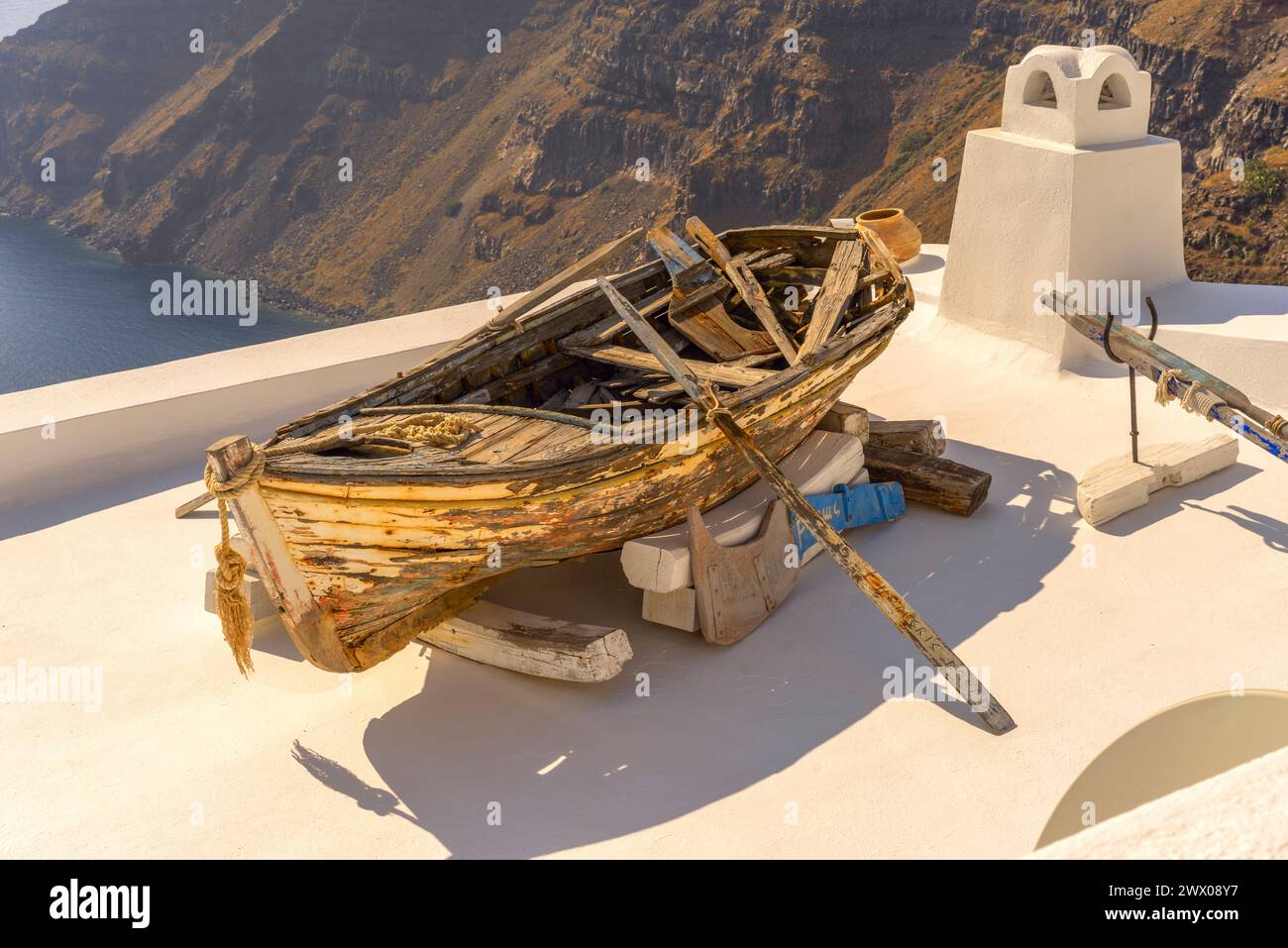 La vecchia barca a remi malandata è usata per decorare l'area di fronte a una dimora che si affaccia sulla Caldera di Santorini e sul Mar Egeo Foto Stock