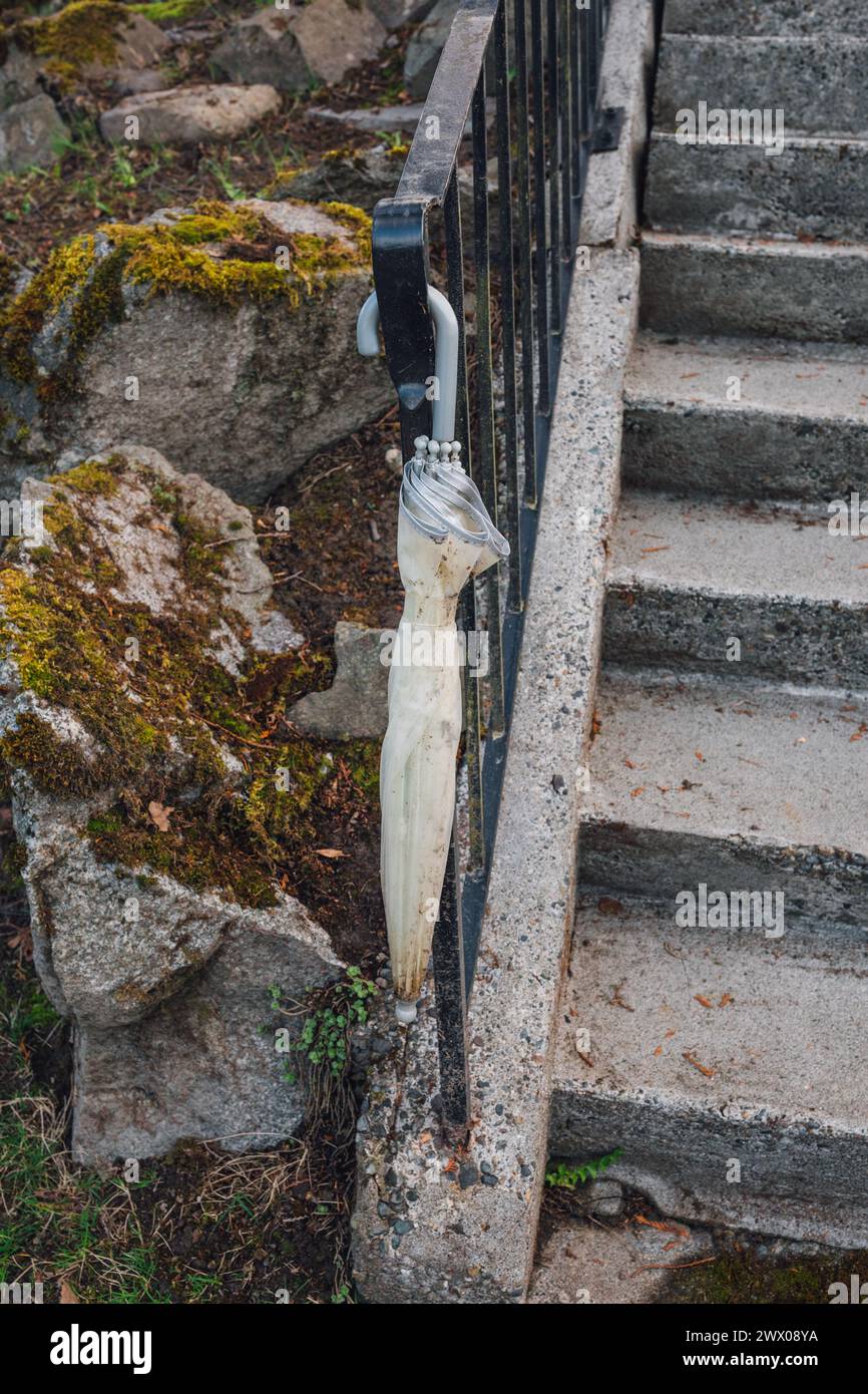 ombrello in plastica grigia sporca riempito d'acqua che si consegna su ringhiera per scale esterne con rocce coperte di muschio Foto Stock