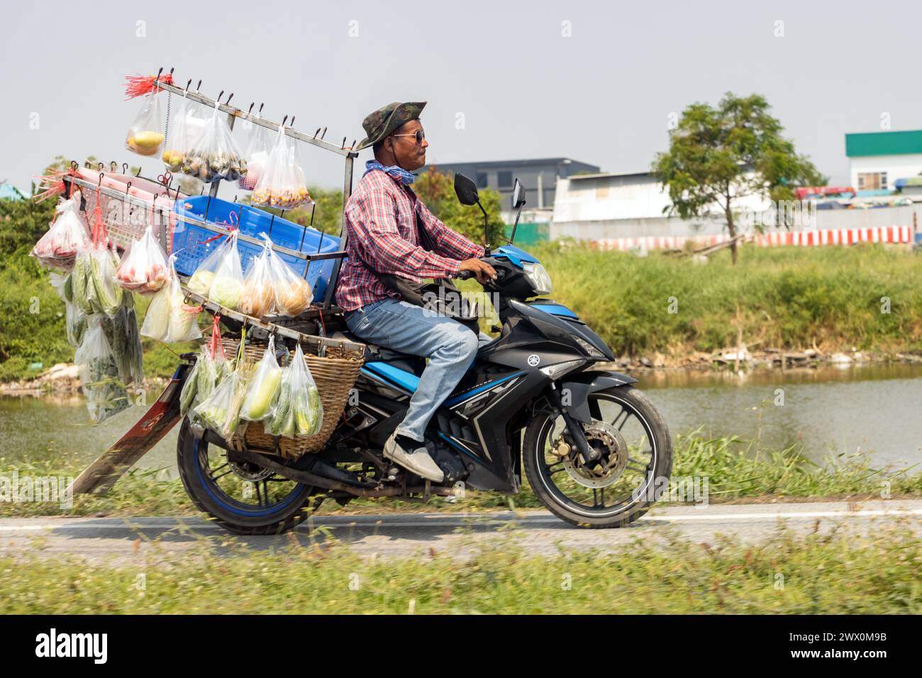 SAMUT PRAKAN, TAILANDIA, FEB 26 2024, Un venditore di frutta e verdura guida con prodotti freschi in moto Foto Stock