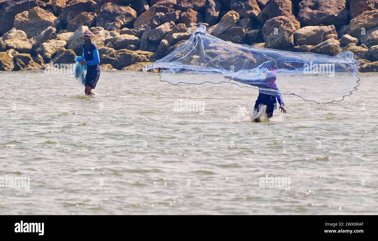 Due pescatori gettano una rete nel mare di fronte a una parete rocciosa nel Golfo della Thailandia Foto Stock