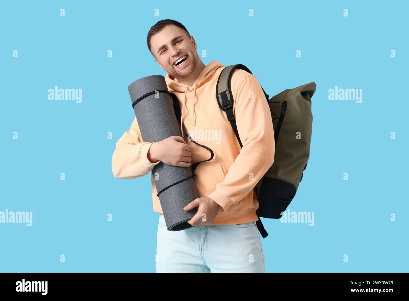 Turista maschile con zaino e tappeto da campeggio su sfondo blu Foto Stock