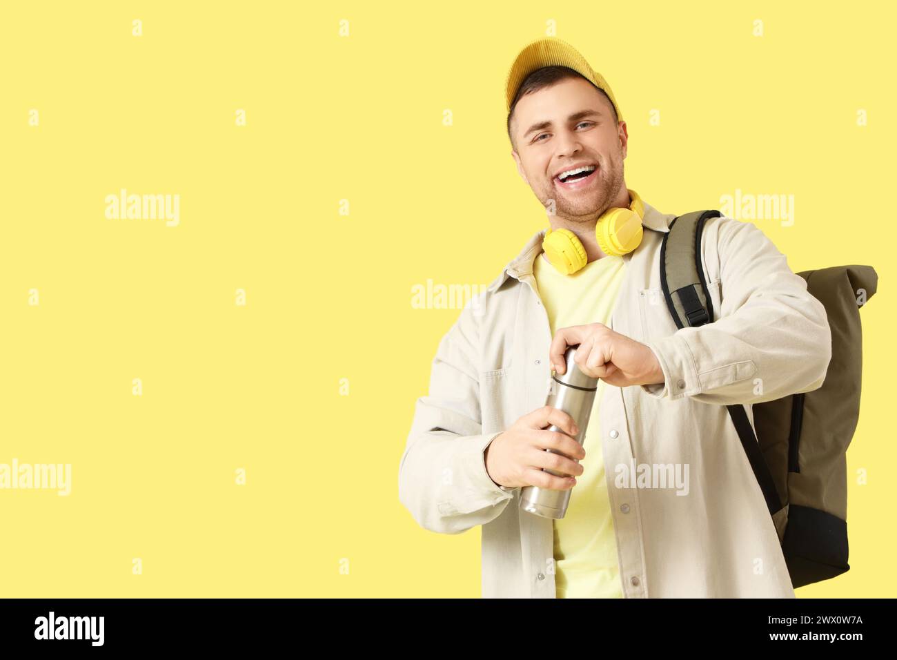 Turista maschile con zaino e thermos su sfondo giallo Foto Stock