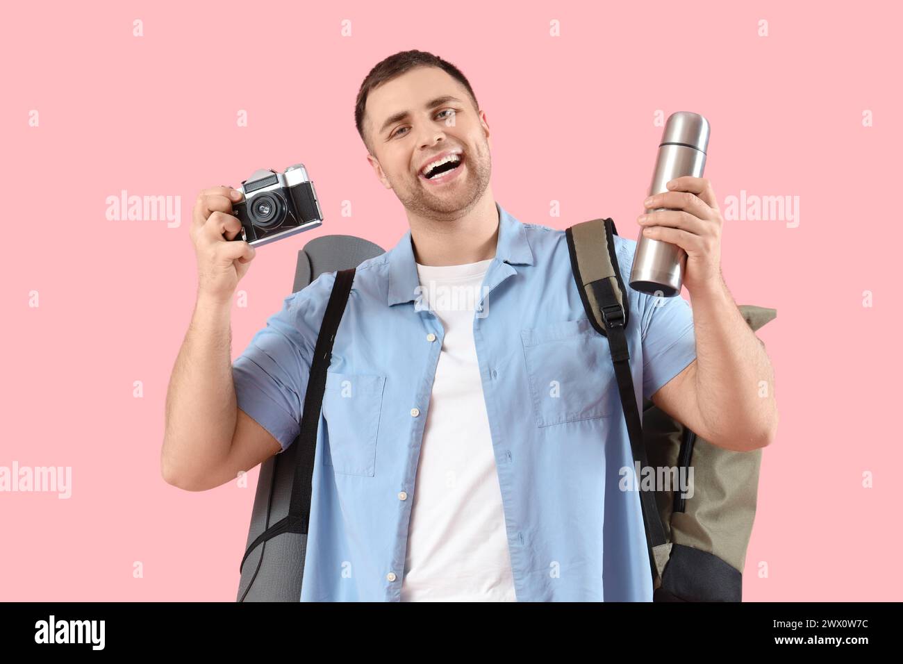 Turista maschile con zaino, thermos e fotocamera su sfondo rosa Foto Stock