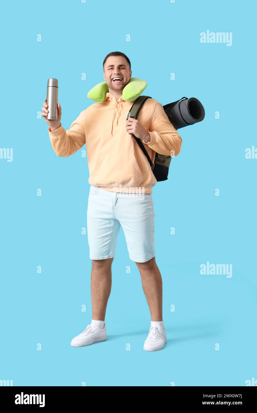 Turista maschile con zaino, tappetino da campeggio e termos su sfondo blu Foto Stock