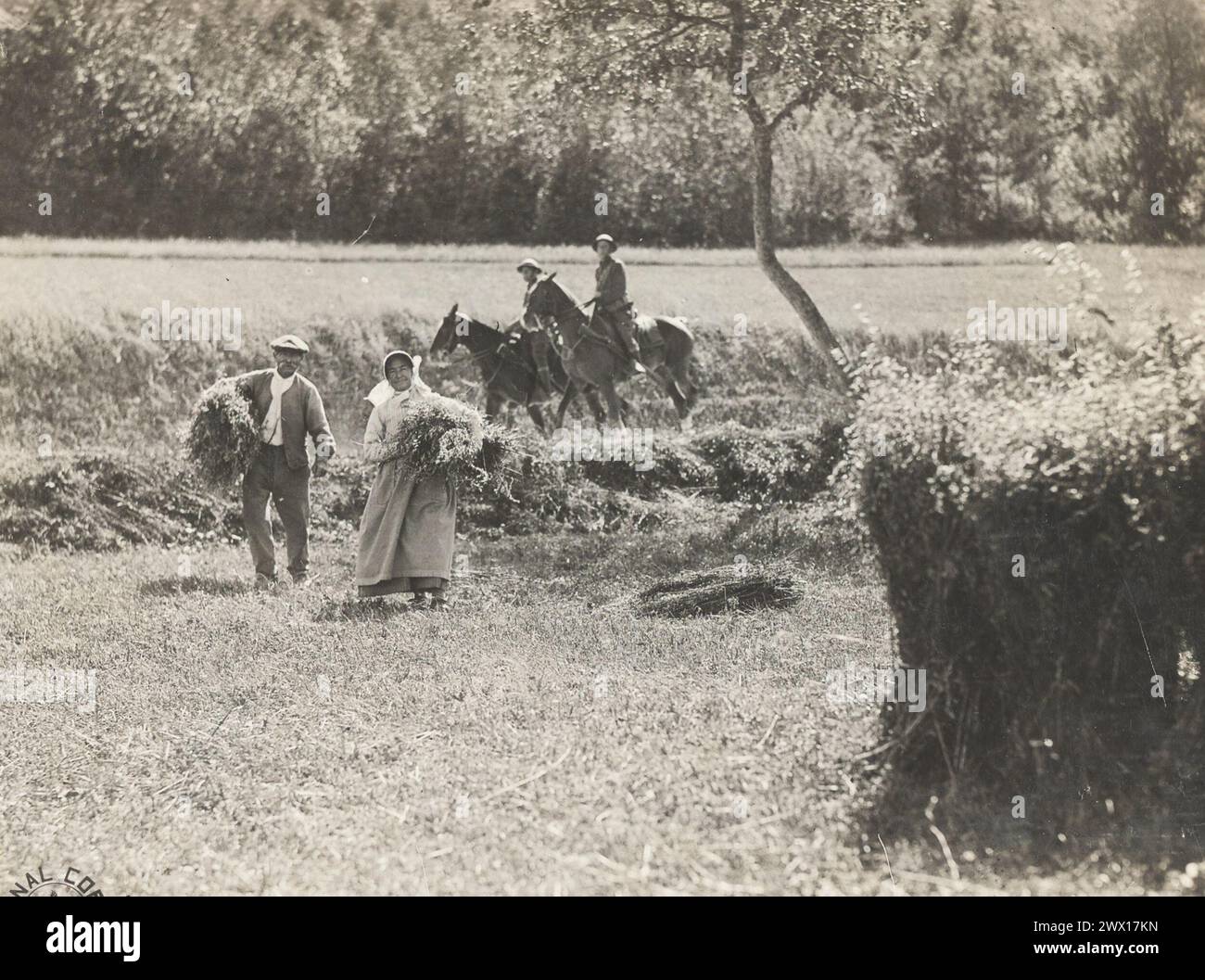 Un uomo e una donna nella loro fattoria che raccolgono con cavalieri di spedizione a cavallo delle truppe del quartier generale, la 33rd Division, possono essere visti passare sullo sfondo; Willencourt Meuse, Francia ca. 1918 Foto Stock