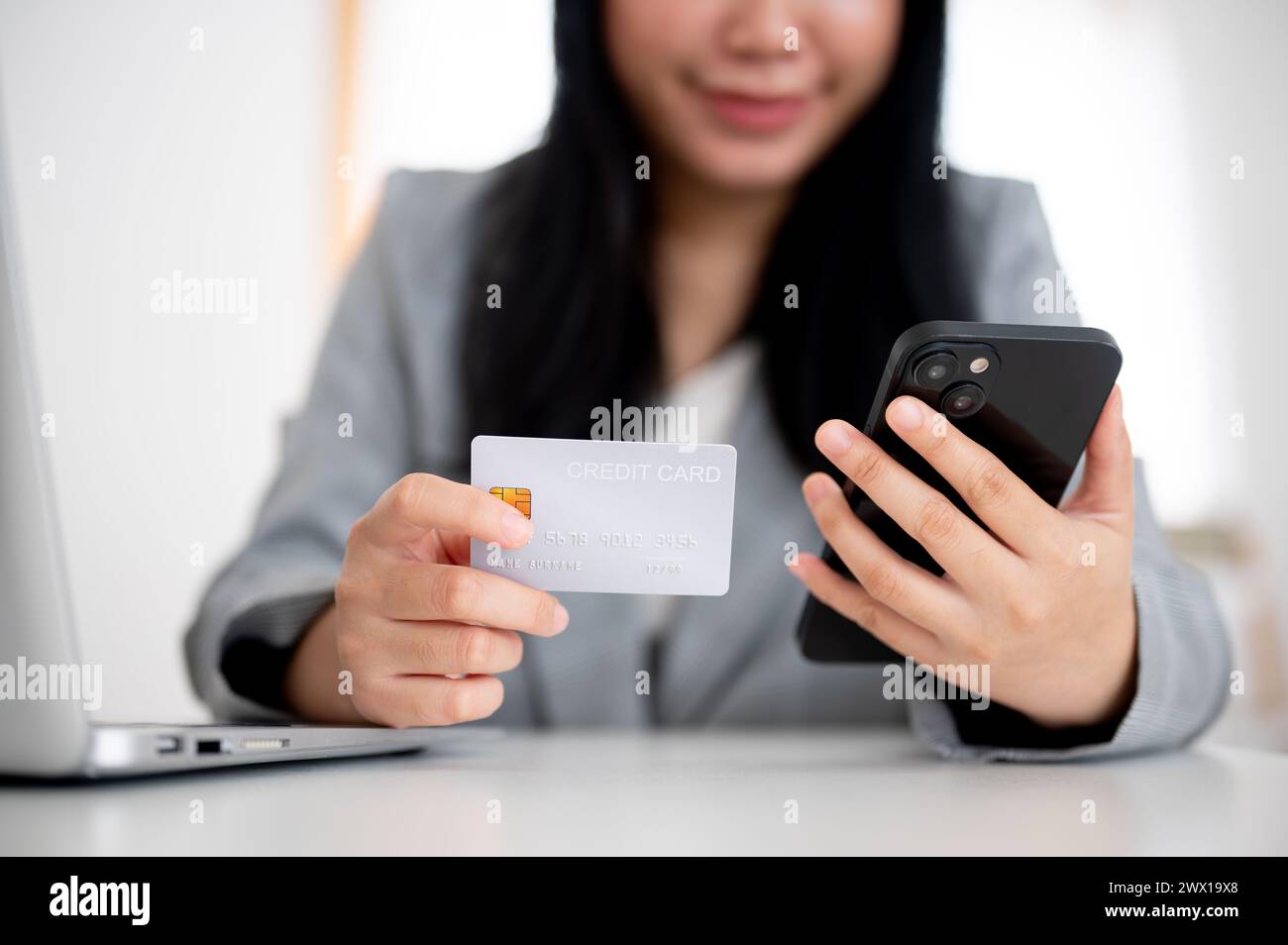 Un'immagine ritagliata di una donna d'affari in un blazer grigio ha in mano uno smartphone e una carta di credito, utilizza il servizio di pagamento online e registra la sua CA di credito Foto Stock