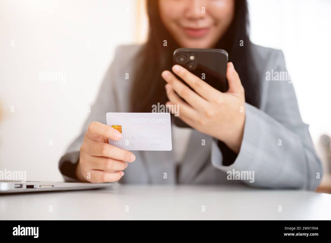 Un'immagine ritagliata di una donna d'affari in un blazer grigio ha in mano uno smartphone e una carta di credito, utilizza il servizio di pagamento online e registra la sua CA di credito Foto Stock