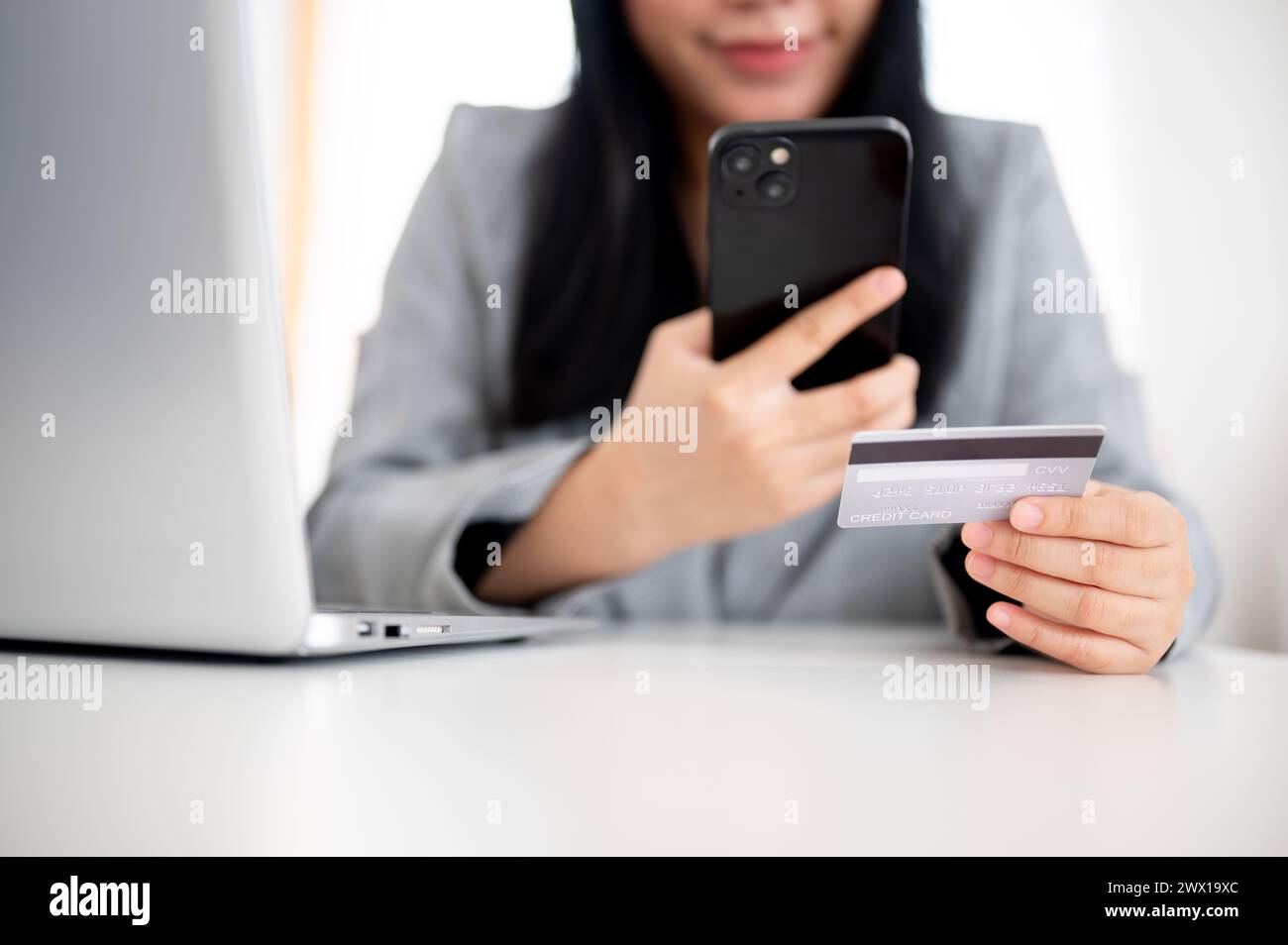 Un'immagine ritagliata di una donna d'affari in un blazer grigio ha in mano uno smartphone e una carta di credito, utilizza il servizio di pagamento online e registra la sua CA di credito Foto Stock