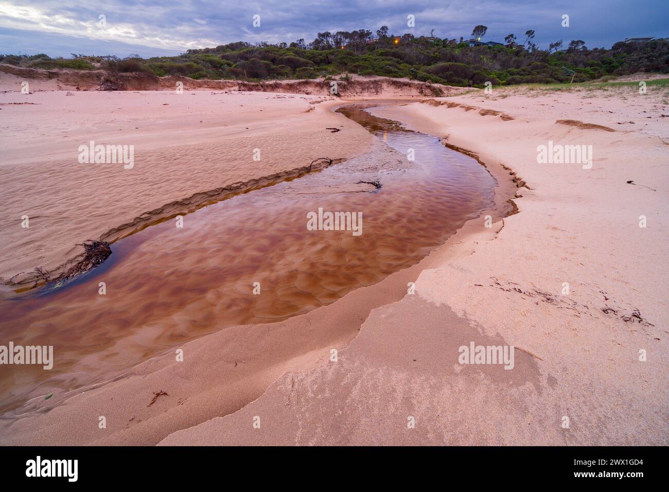 Un torrente costiero che scorre su una spiaggia sabbiosa durante il crepuscolo a Cape Paterson a Gippsland, Victoria, Australia. Foto Stock