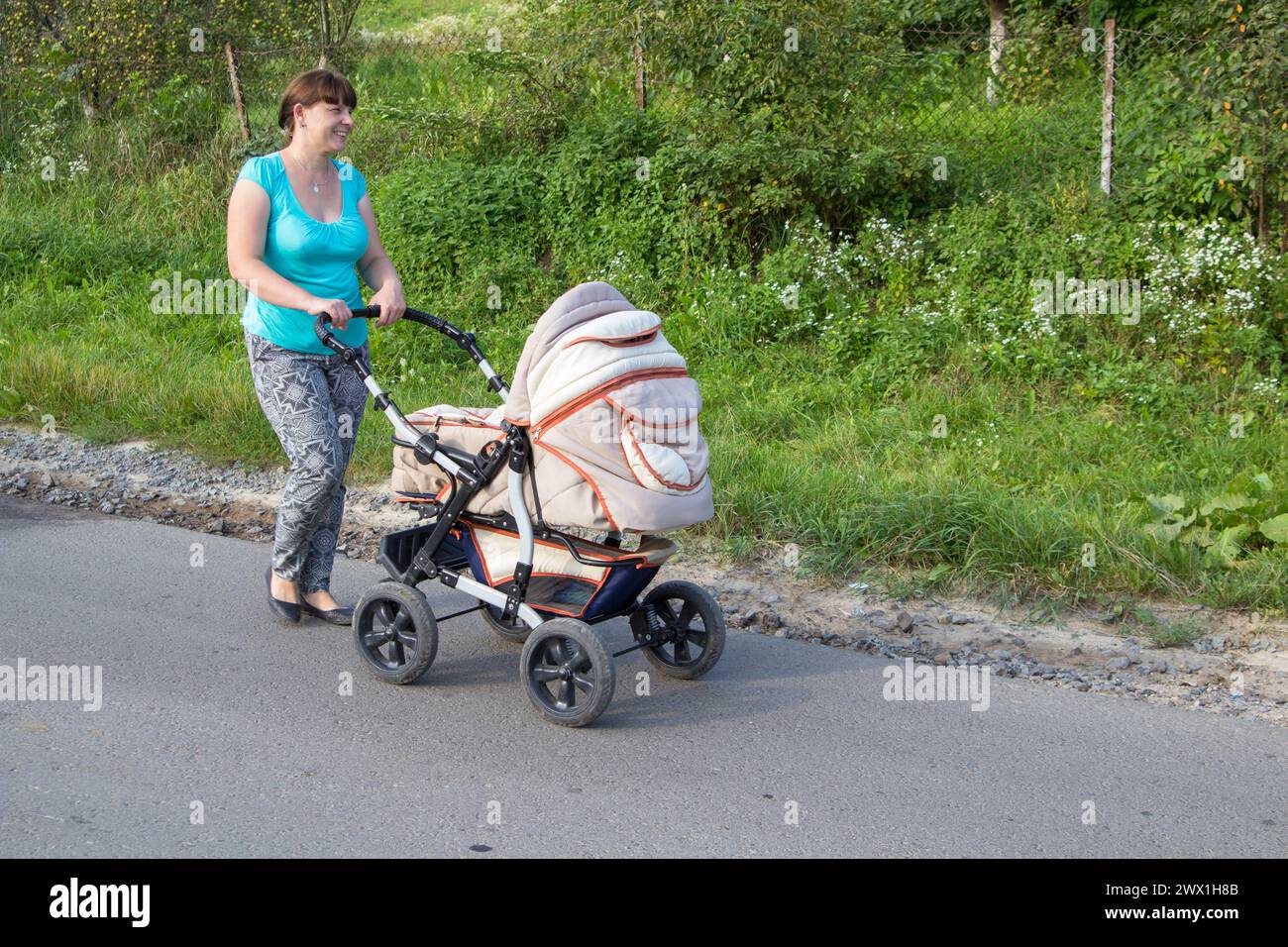 donna felice che cammina per strada con un passeggino in estate Foto Stock