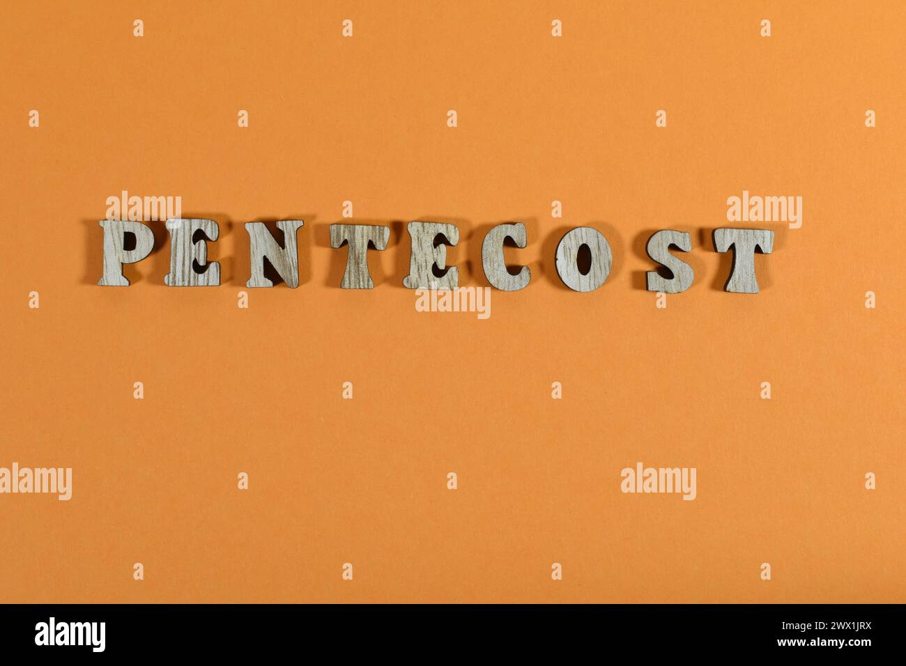 La parola Pentecoste fatta di lettere di legno su sfondo arancione Foto Stock