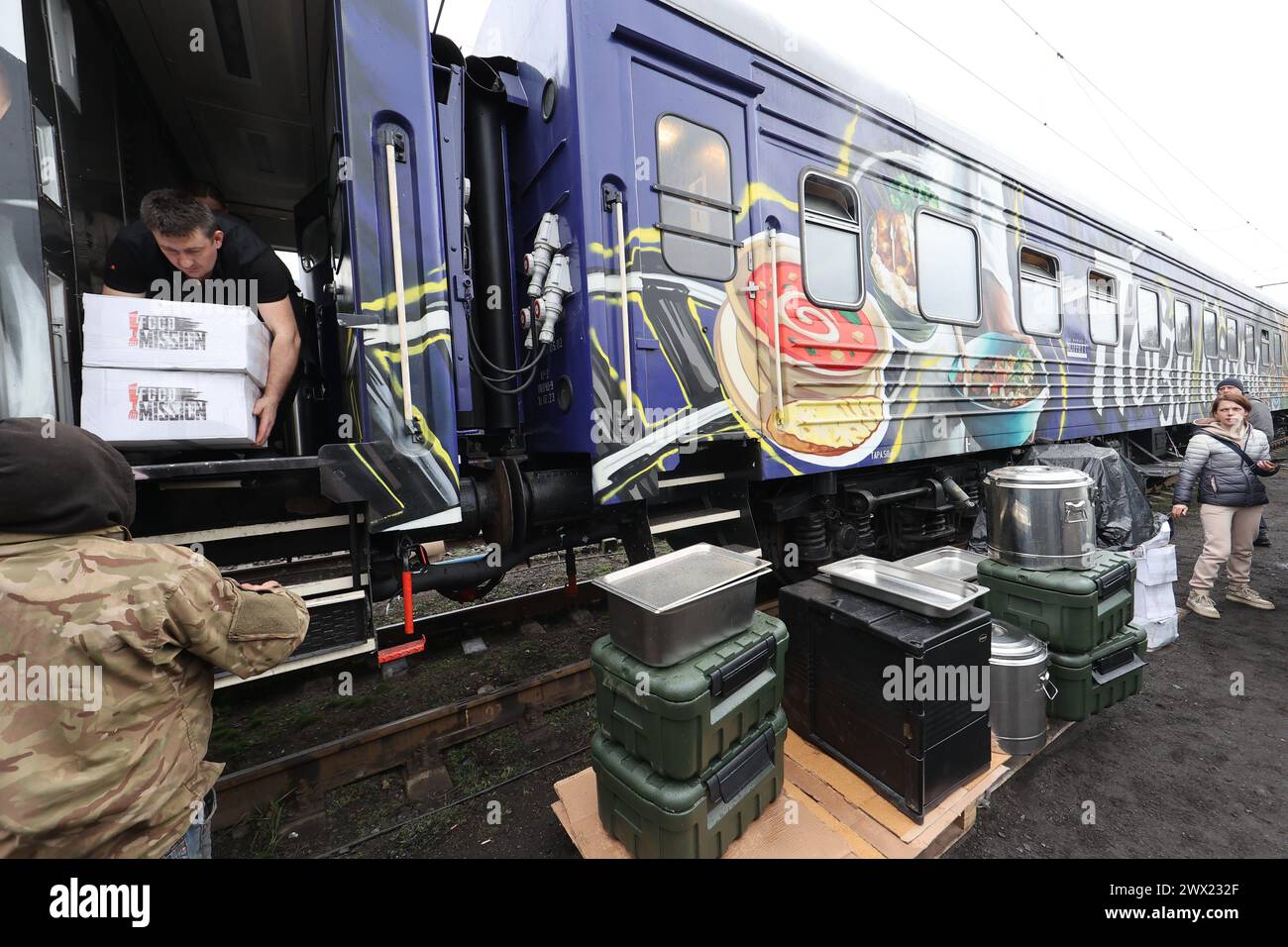 CHARKIV, UCRAINA - 26 MARZO 2024 - volontari e lavoratori della società della Croce Rossa Ucraina ricevono pranzi per i pazienti di ospedali e sfollati interni che vivono in ostelli presso il treno alimentare che è arrivato in città e soffre di interruzioni di corrente causate dagli attacchi russi alle infrastrutture critiche, Charkiv, Ucraina nord-orientale. Il treno alimentare è un progetto delle Ferrovie ucraine (Ukrzaliznytsia) che è stato implementato con la fondazione del miliardario americano Howard Buffett. Il treno della cucina può produrre più di 10.000 porzioni di cibo al giorno, anche in assenza di energia. Foto Stock