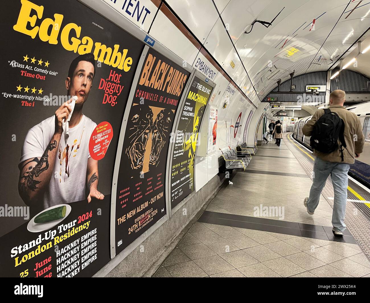 Un poster che pubblicizza il tour Hot Diggity Dog di ed Gamble sulla piattaforma della Bakerloo line alla stazione della metropolitana Embankment a Londra. Il comico ed Gamble è stato costretto a rimuovere una foto di un hot dog dai suoi poster dopo aver violato la politica pubblicitaria di TfL sulla presenza di cibi ricchi di grassi, zucchero e sale. Il comico ha invece scambiato l'hot dog con un cetriolo per ottenere il materiale promozionale in mostra. Data foto: Mercoledì 27 marzo 2024. Foto Stock