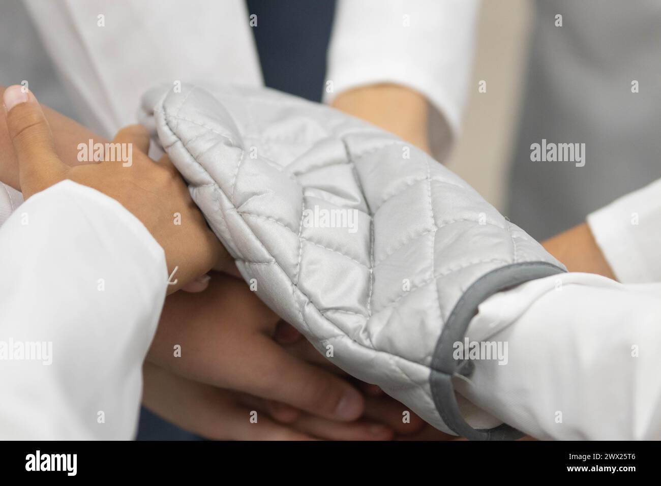 Primo piano di mani in un esperimento scientifico scolastico durante la lezione. Uno dei bambini può essere visto indossare un guanto da forno. Foto Stock